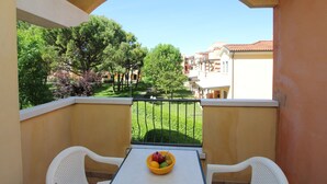 Ein Balkon mit Tisch und Stühlen, einer Obstschale und Blick auf einen Garten und Gebäude.