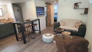 A modern living room with a sofa, a brown armchair, a coffee table, and a dining area with a bar stool and a TV. - The Bird of Paradise (Entre-Deux)