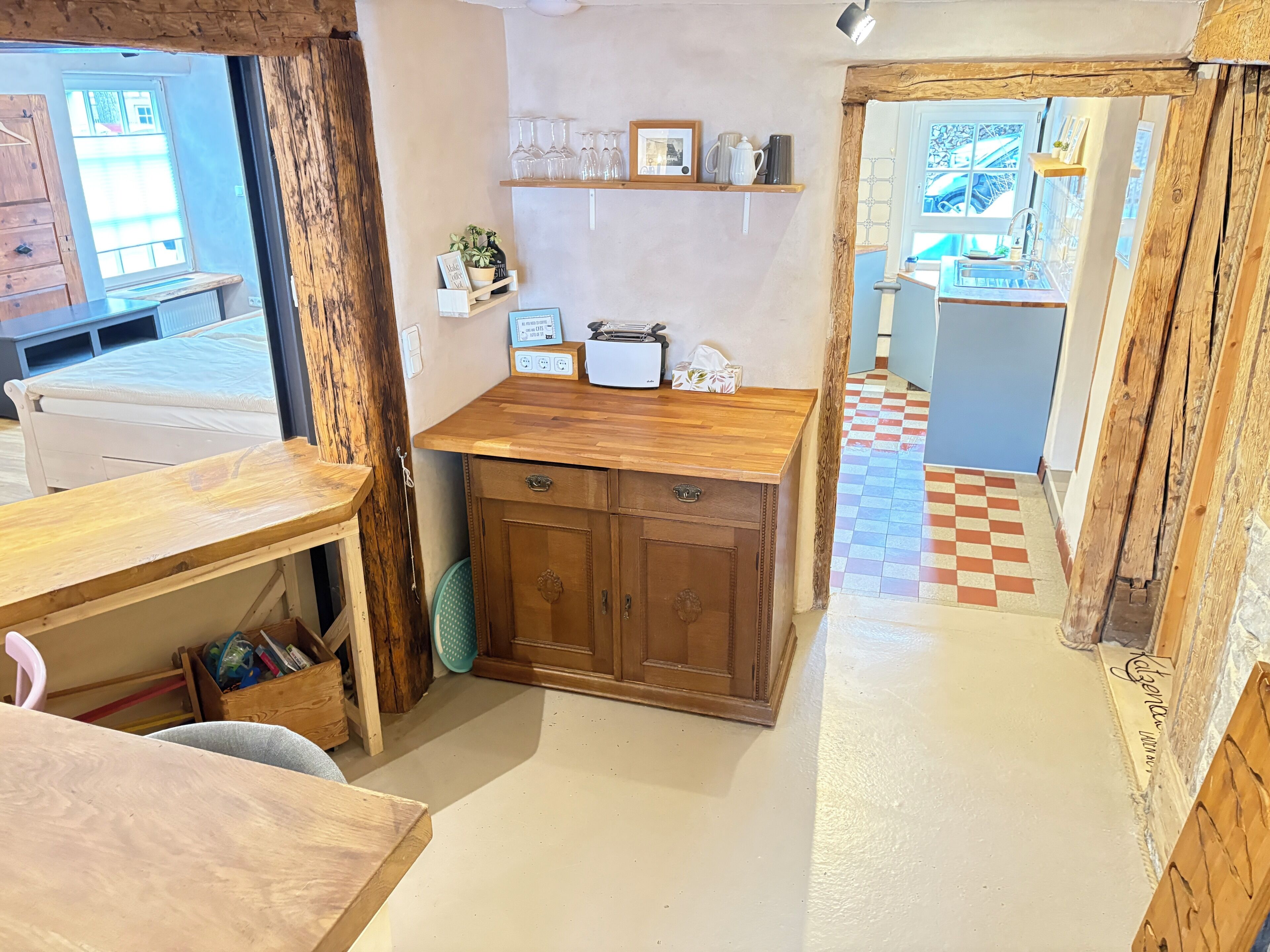 A compact kitchen with wooden cabinets, a countertop, and a window. There is a shelf with glasses and a framed picture.