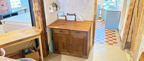 A compact kitchen with wooden cabinets, a countertop, and a window. There is a shelf with glasses and a framed picture.