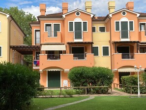Un immeuble résidentiel à plusieurs étages, doté de balcons, d’un patio couvert et d’un jardin bien entretenu.