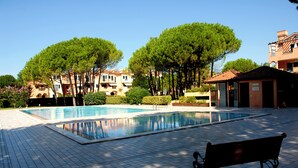 A swimming pool with tiled flooring, surrounded by trees and buildings. - Seaside Apartment With Shared Pool (San Michele al Tagliamento)