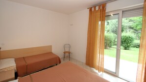 Habitación de hotel con dos camas, una silla y puerta corrediza de cristal a un jardín.