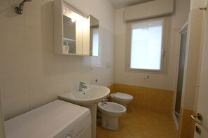Een badkamer met een wastafel, bidet, toilet en een douchegedeelte.