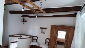 Ein Zimmer mit freiliegenden Holzbalken, einem weißen Schrank mit Spiegel, zwei Stühlen, einem kleinen Tisch und einem großen Teppich.