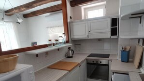 Eine kleine Küche mit weißen Schränken, einer Holzbalkendecke und einem Schachbrettmuster-Teppich.