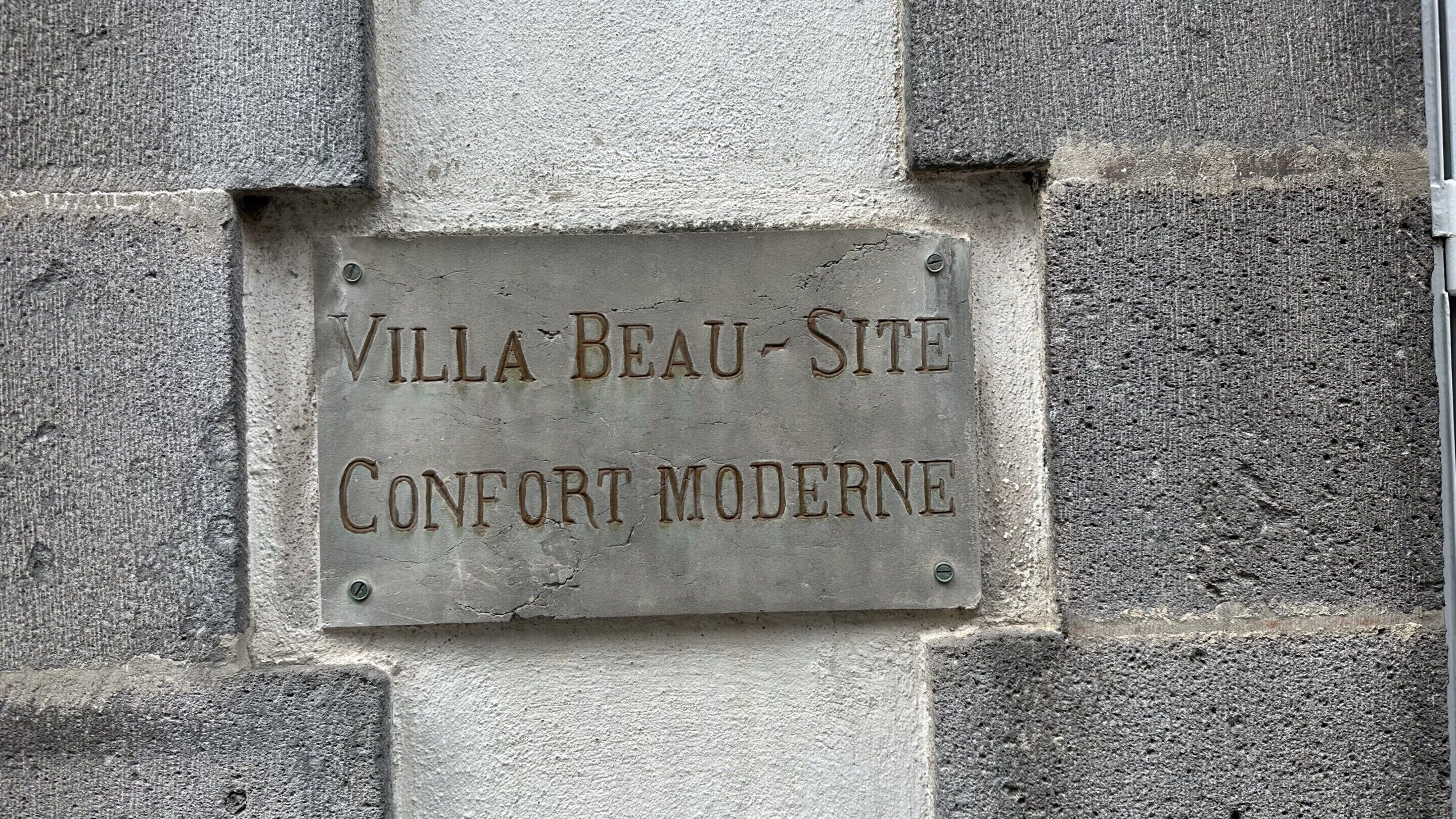 Una placa con el texto 'VILLA BEAU-SITE CONFORT MODERNE' colocada en una pared de piedra.
