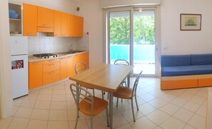 Eine kompakte Küche mit orangefarbenen Schränken, einem Esstisch mit Stühlen und einem blauen Sofa in einem hellen Zimmer mit einem großen Fenster.