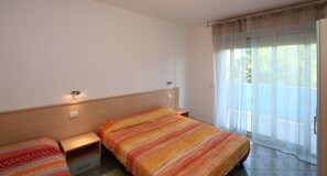 Ein Hotelzimmer mit zwei Betten, einem hölzernen Kopfteil, einem kleinen Nachttisch und einem Fenster mit durchsichtigen Vorhängen.