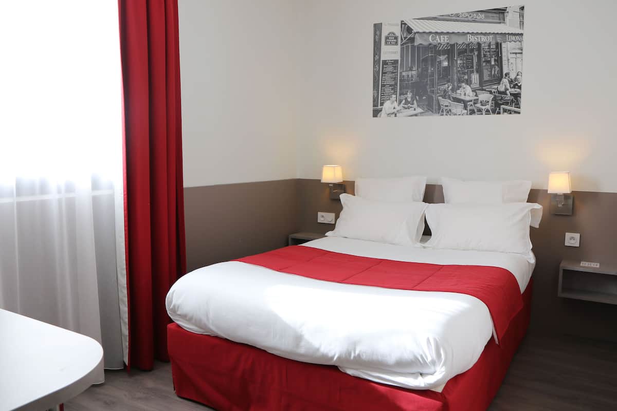 Habitación de hotel con cama, dos lámparas de noche, una mesa y un cuadro en la pared.