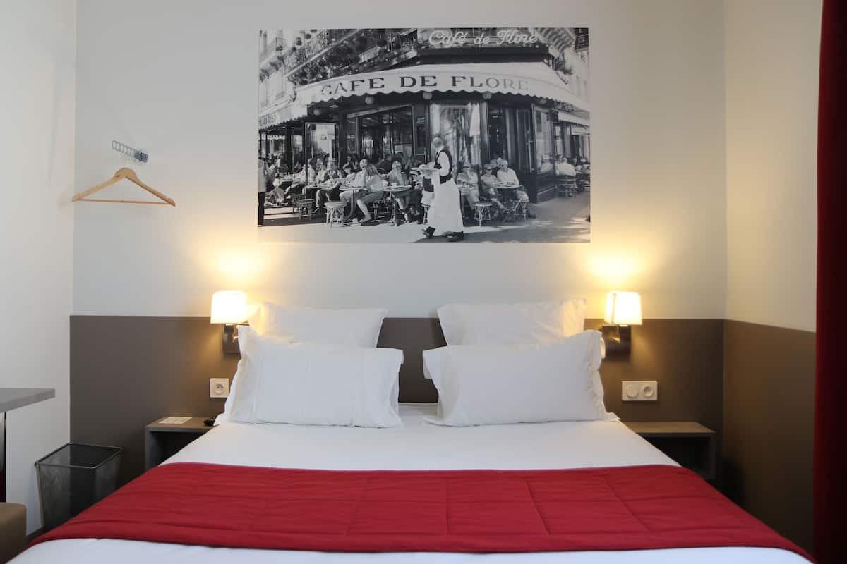 Habitación de hotel con una cama, dos mesitas de noche, una manta roja y un cartel de un café.
