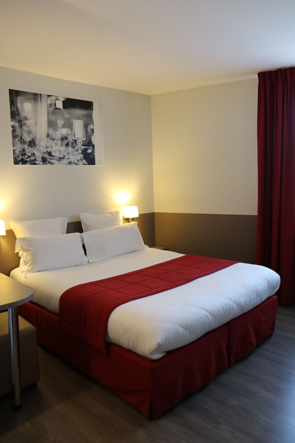 A hotel room with a large bed, two bedside lamps, a red bed runner, and a framed picture on the wall. - Le Quarré (Bruguières)