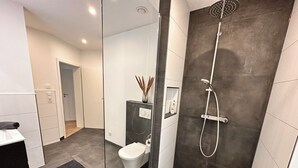 A modern bathroom with a glass partition, a shower, a toilet, and a sink.