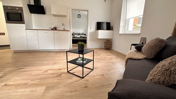A modern living space with a kitchen, a dining area, and a seating area with a sofa and a coffee table.