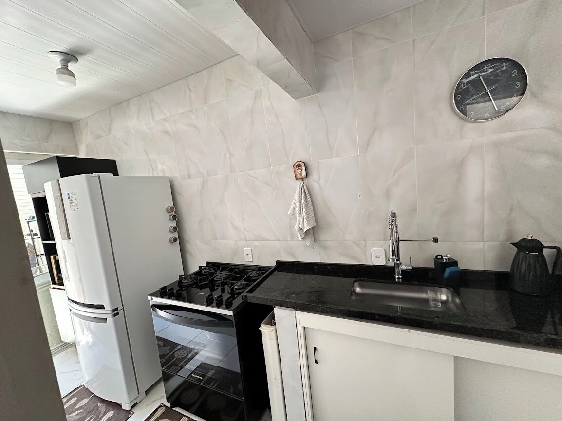 Eine Küche mit weißen Schränken, einer schwarzen Arbeitsplatte, einem Spülbecken, einem Herd und einem Kühlschrank.