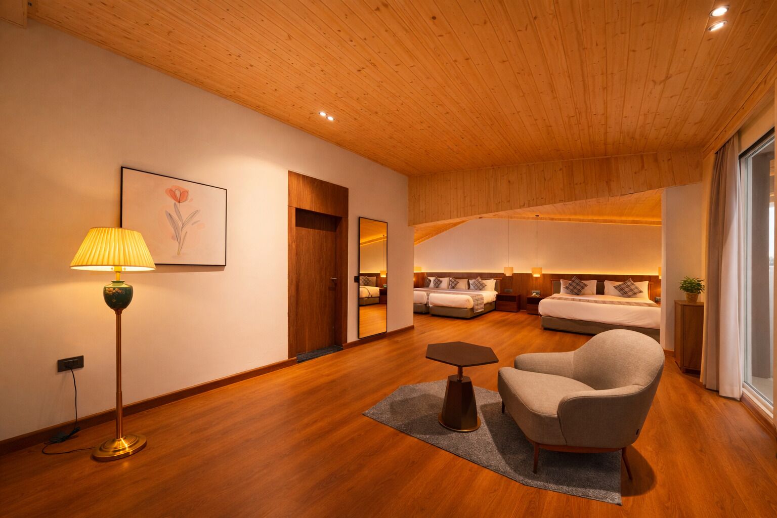 A modern hotel room with wooden flooring, a sofa, a lamp, and a bed with a headboard.