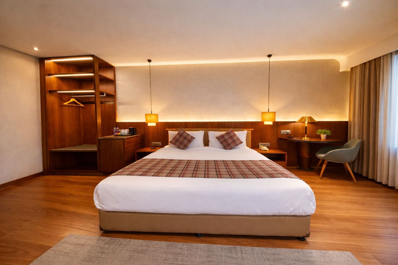 Quarto de hotel com uma cama grande, mesas de cabeceira, uma escrivaninha, uma cadeira, um guarda-roupa e um cabideiro.