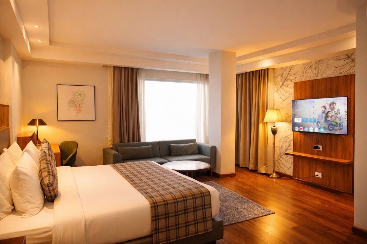 A hotel room with a bed, a sofa, a TV, and a window with curtains.