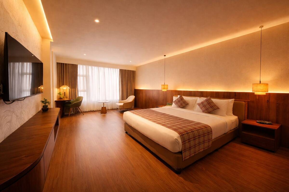 A hotel room with a large bed, a desk, a chair, a TV, and a window with curtains.