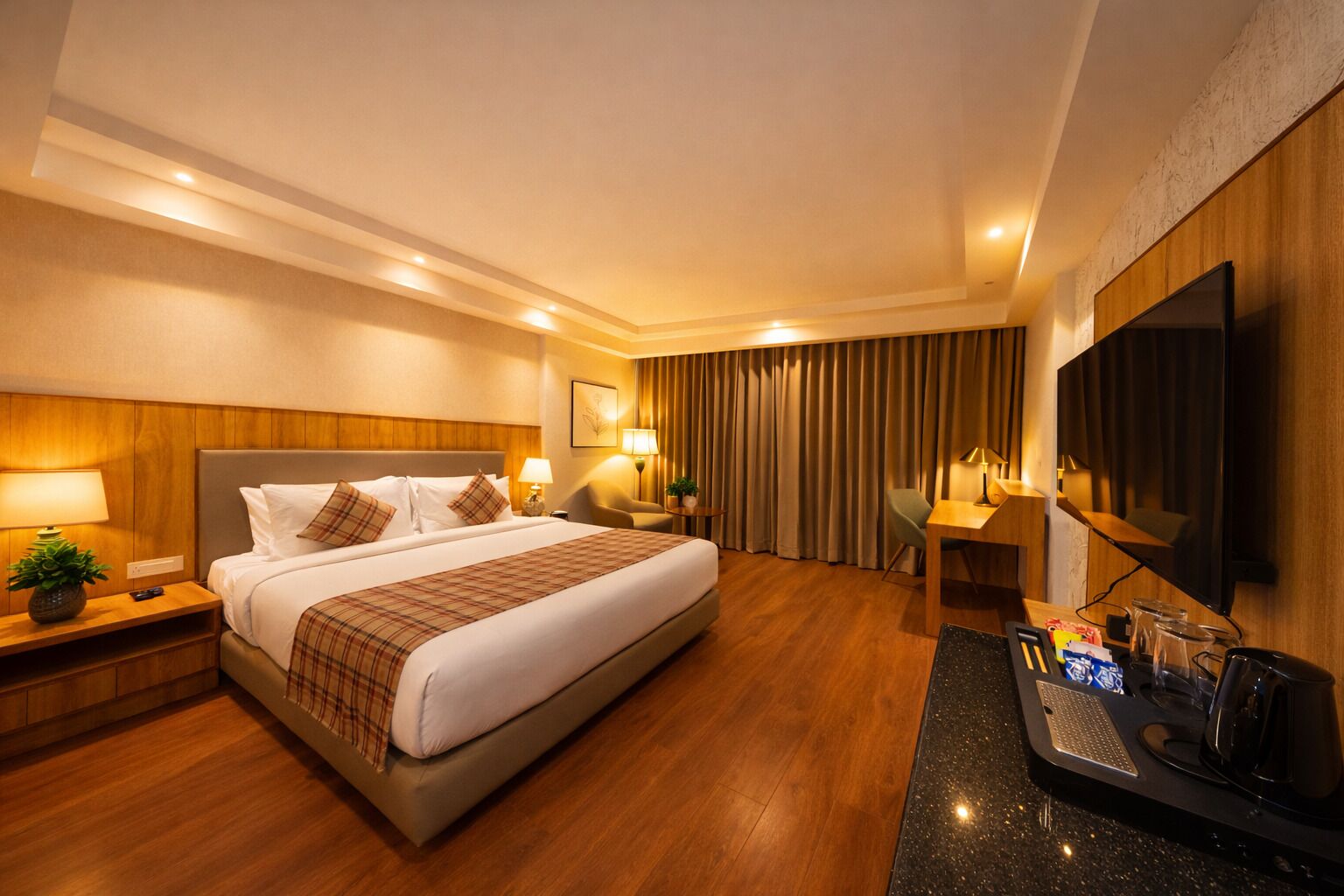 A hotel room with a large bed, bedside tables with lamps, a desk with a chair, a flat-screen TV, and a coffee station.