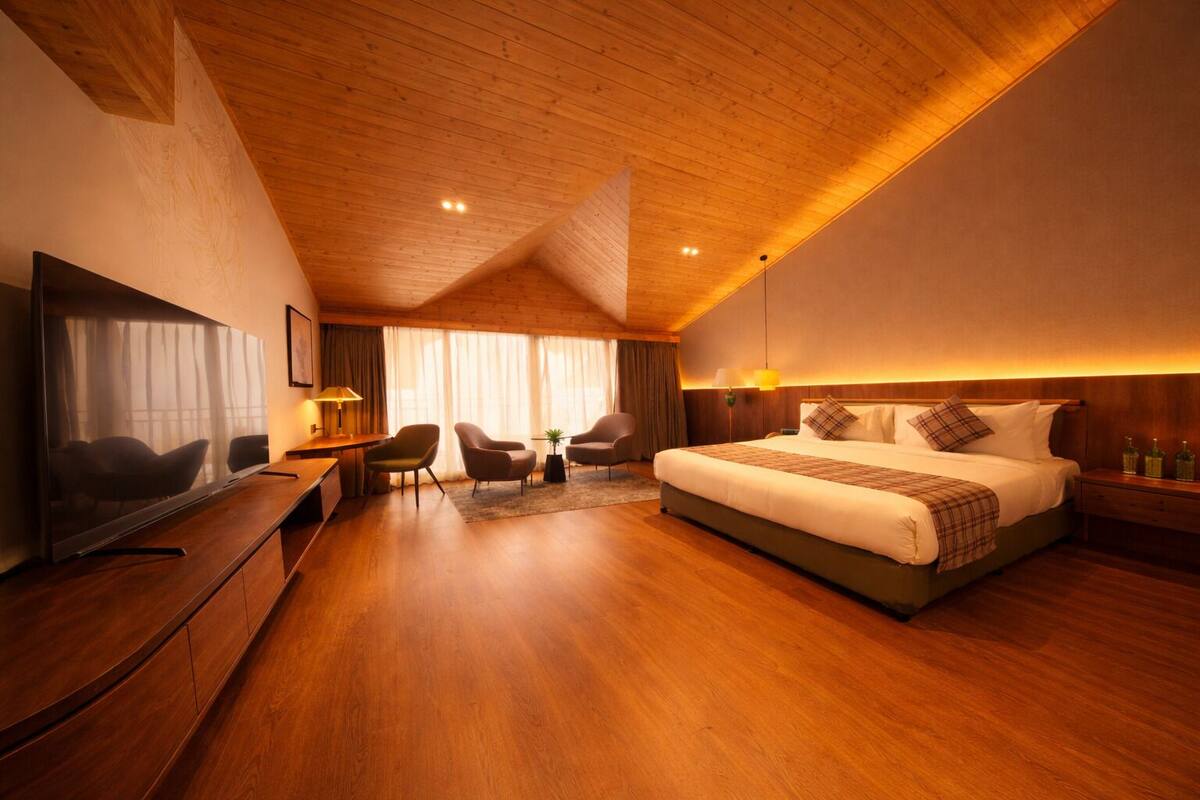 A hotel room with a large bed, a desk, a chair, a TV, and a window with curtains.