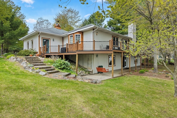A two-story house with a porch, a staircase leading to the entrance, and a swing chair.