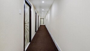 Een lange, smalle hotelgangen met een patroon vloerkleed, witte muren en deuren met decoratieve glaspanelen.