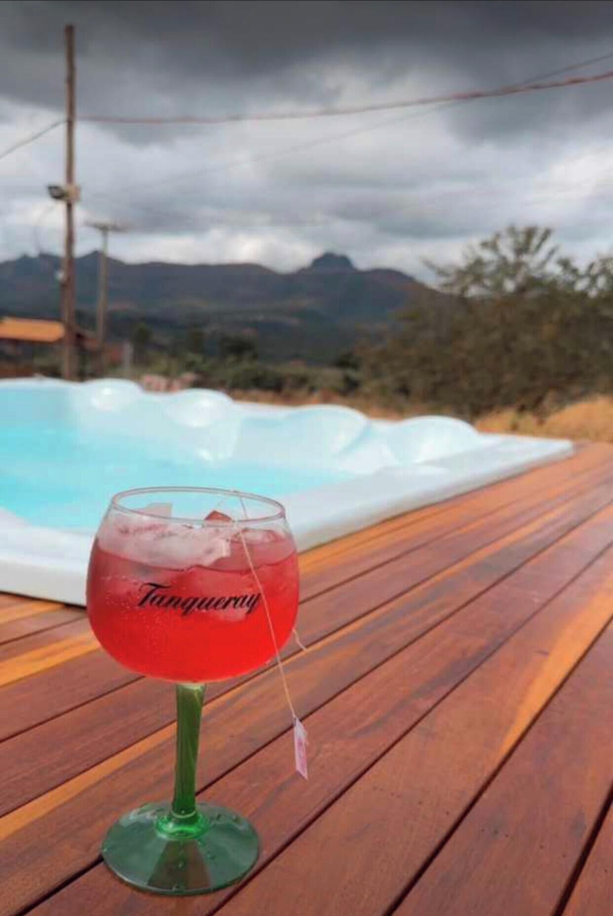 A glass of red drink on a wooden deck with a hot tub in the background.