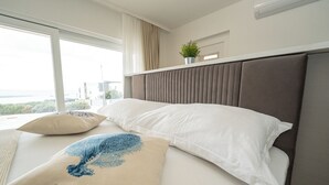 Quarto de hotel com uma cama grande, vista para a cidade e uma planta em vaso no criado-mudo.