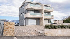 Um edifício residencial de vários andares com design moderno, com varandas, garagem e acesso pavimentado.