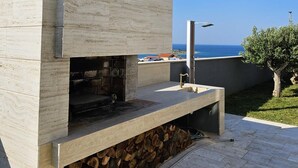 Cozinha externa moderna com fachada de pedra, churrasqueira embutida e vista para o mar.