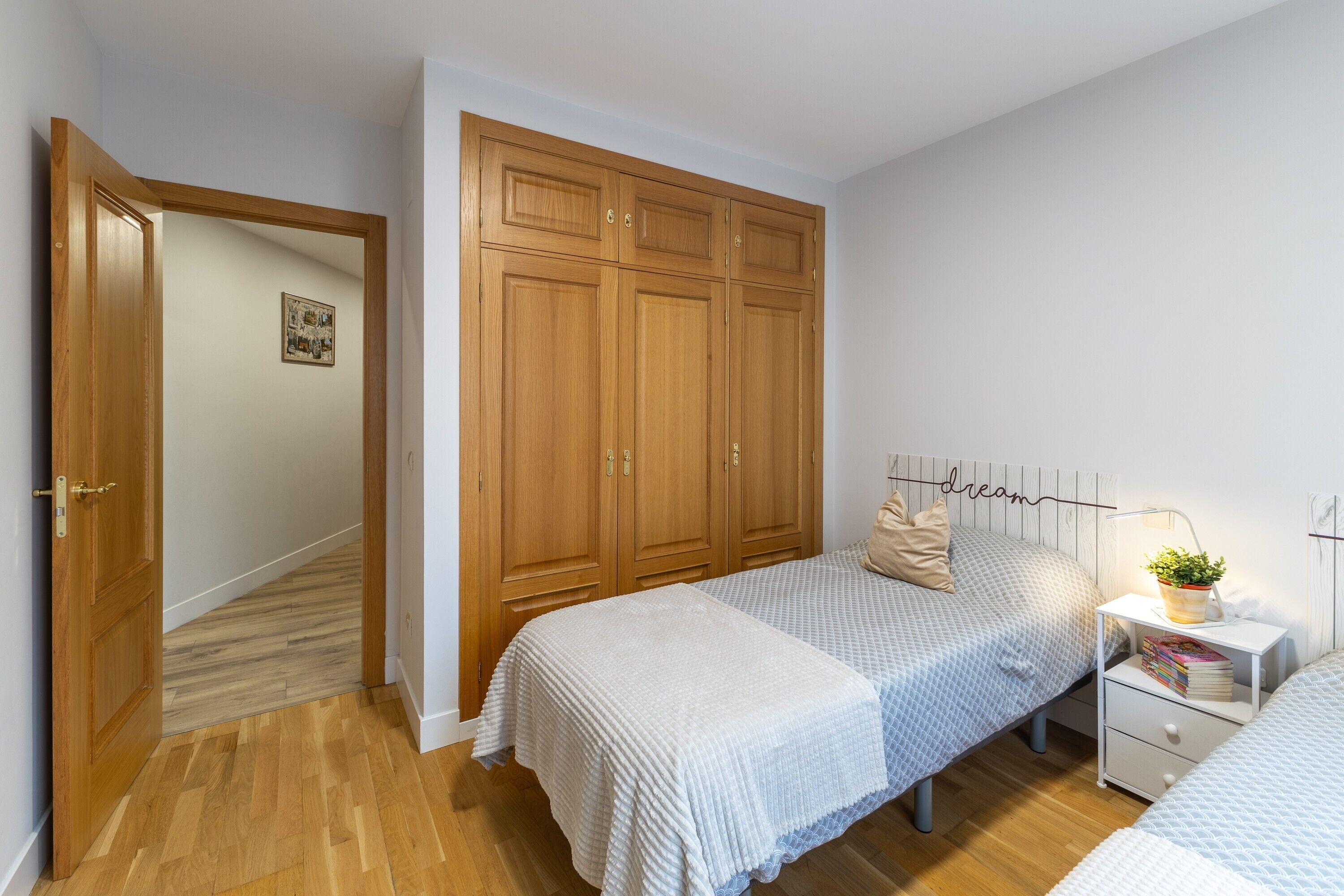 Une chambre à coucher avec une armoire en bois, deux lits, une table de chevet avec une lampe et une petite plante sur la table de chevet.