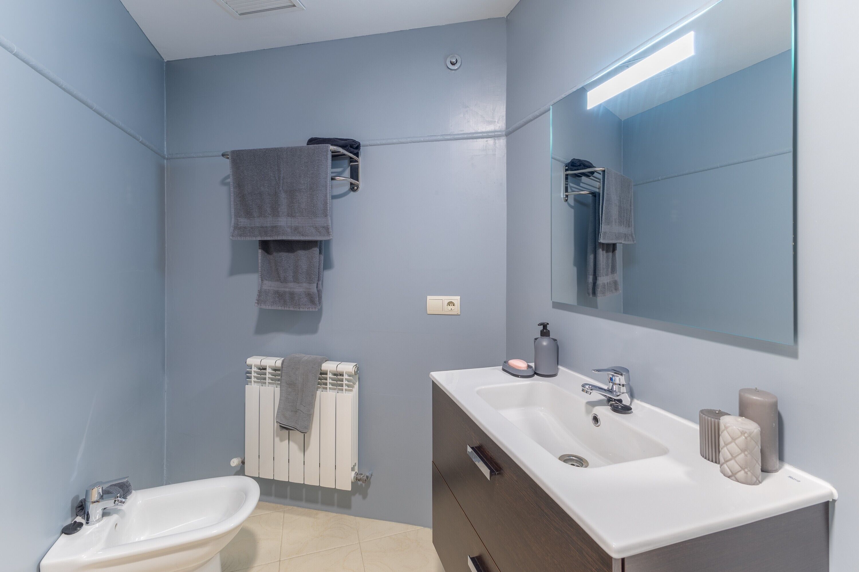 A bathroom with a sink, mirror, towel rack, and radiator.