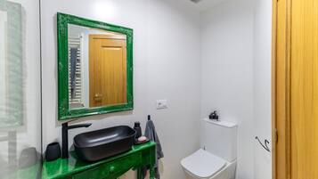 Een badkamer met een groen badkamerkastje, een zwarte wastafel, een spiegel met groene lijst, een wit toilet en een klein plankje met toiletartikelen.