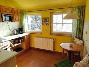 A kitchen with a stove, microwave, and a dining area with a table and chairs. - Apartment Zimt-Apfel direkt an der Piste und am Rothaarsteig gelegen (Winterberg)