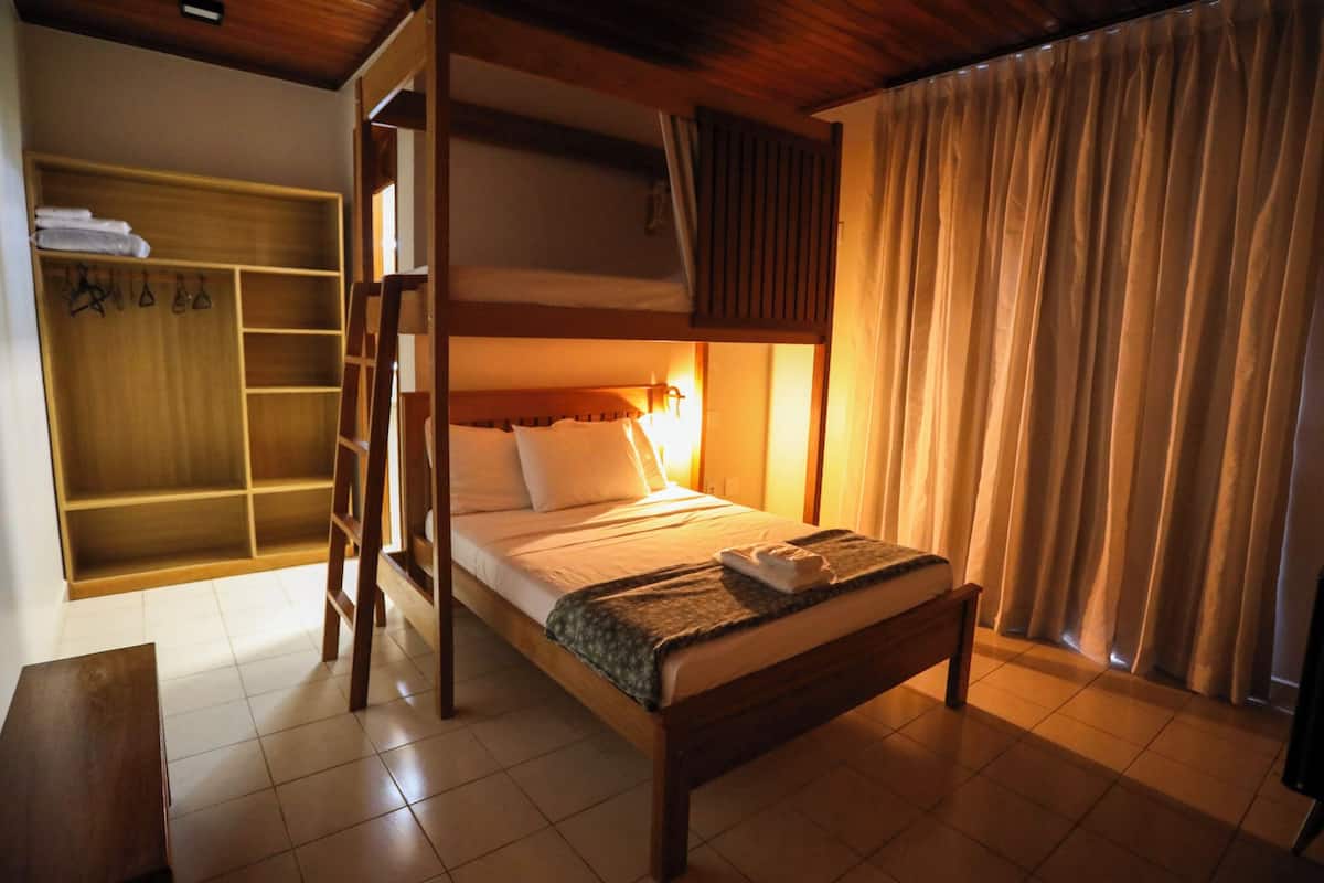 A bunk bed with a ladder, a bedside table, a wooden wardrobe, and a curtain.