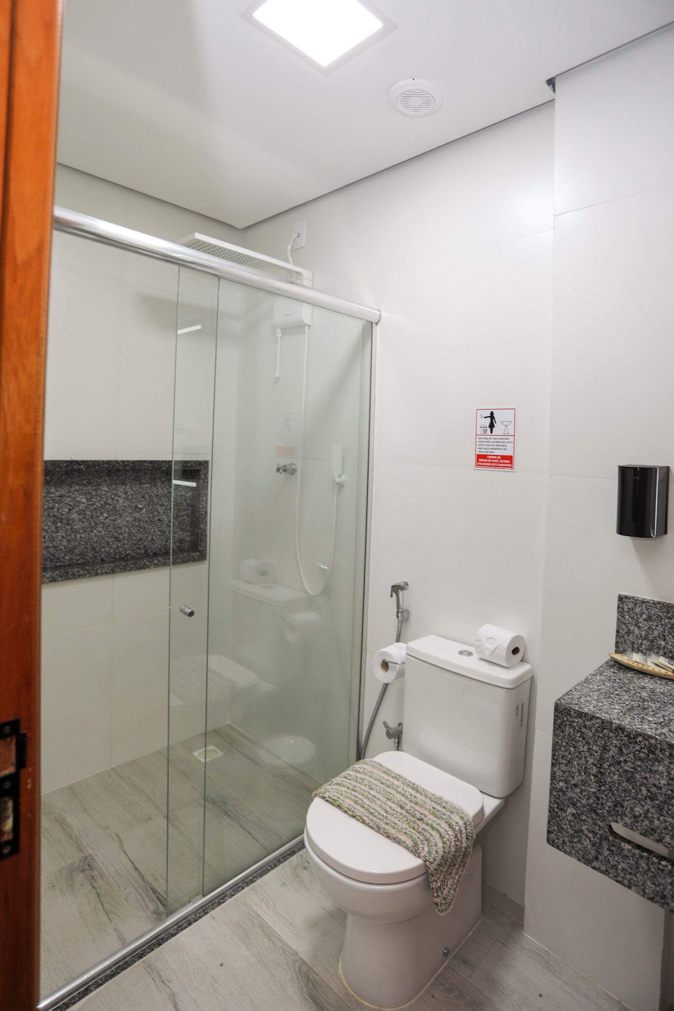 Un baño moderno con ducha envuelta en vidrio, inodoro con toalla y encimera de granito.