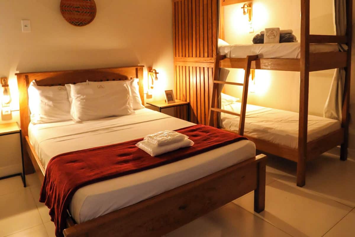 A hotel room with a wooden bunk bed, a single bed with white bedding, a red throw blanket, and two bedside lamps.