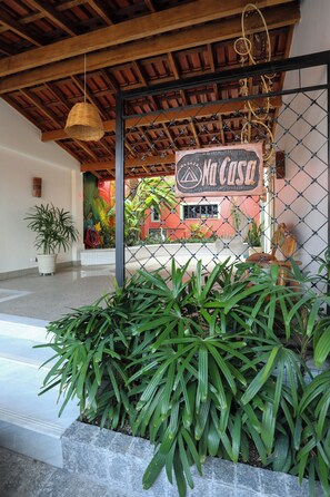A hotel entrance with a sign reading 'Na Casa,' a wooden ceiling, potted plants, and a tiled floor. - Na Casa Hostel (Manaus)