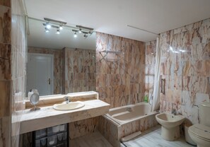 Un baño moderno con paredes de mármol, un lavamanos doble, una bañera, un bidé y un inodoro.