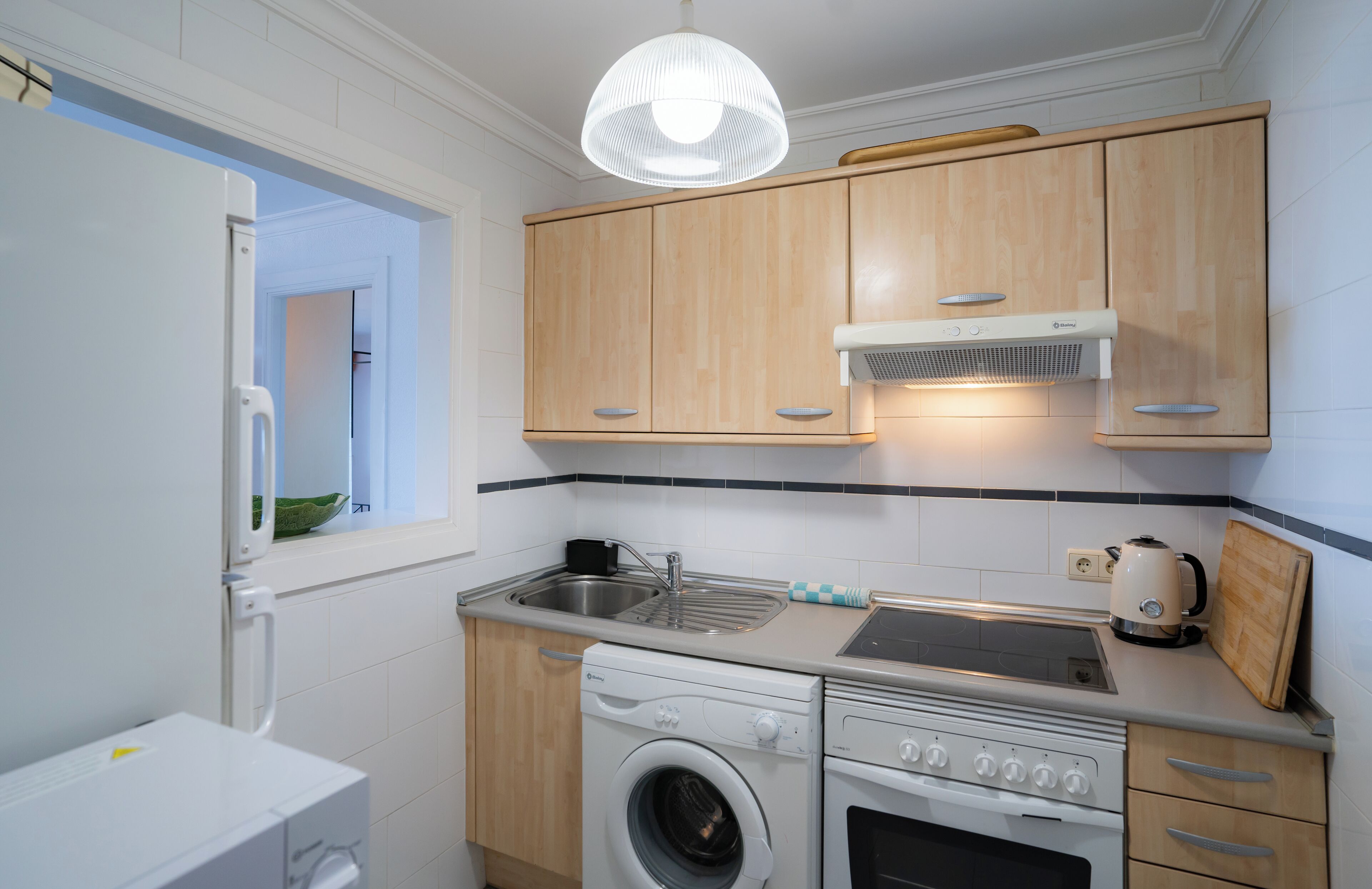 A compact kitchen with wooden cabinets, a built-in oven, a washing machine, and a sink.