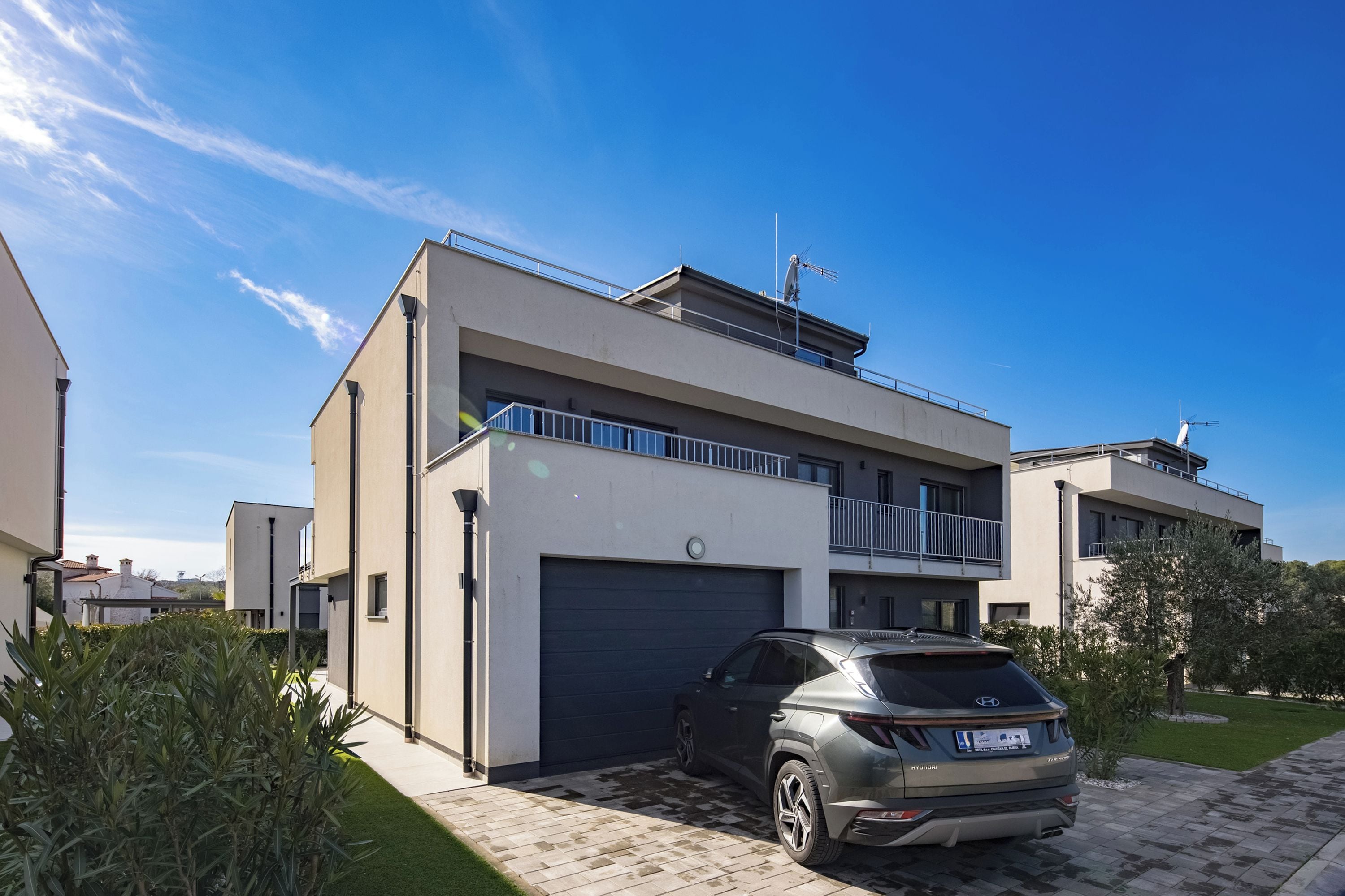 Een modern huis met twee verdiepingen, een garage, een balkon en een geparkeerde SUV.