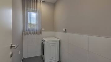 A compact laundry room with a washing machine, a door with a handle, and a window with sheer curtains.