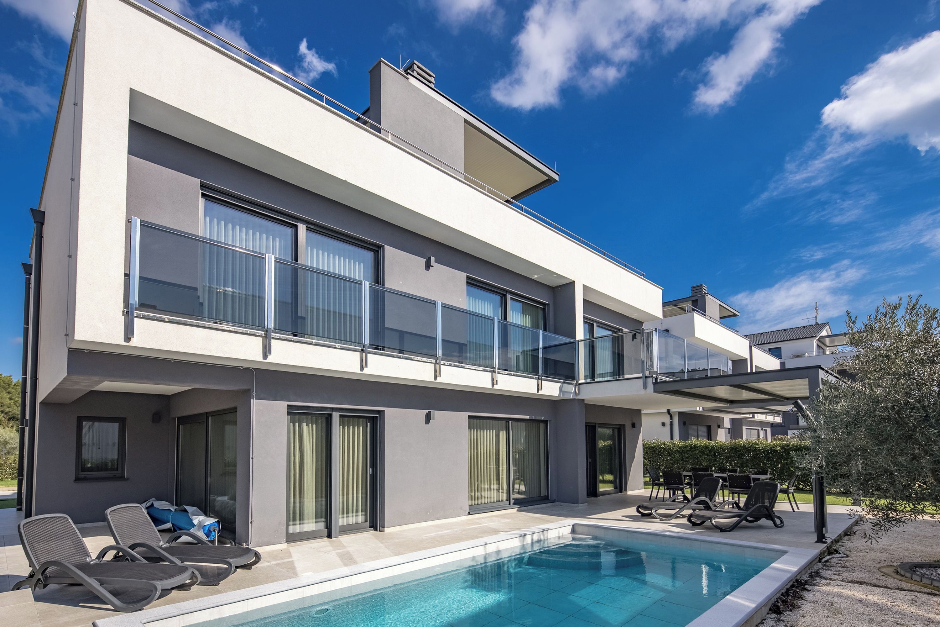 A modern two-story house with a swimming pool, outdoor seating, and a balcony.