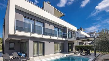 A modern two-story house with a swimming pool, outdoor seating, and a balcony.