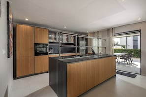 A modern kitchen with wooden cabinets, a central island, and a dining area with a table and chairs. - Villa Centinera With Private Pool (Medulin)