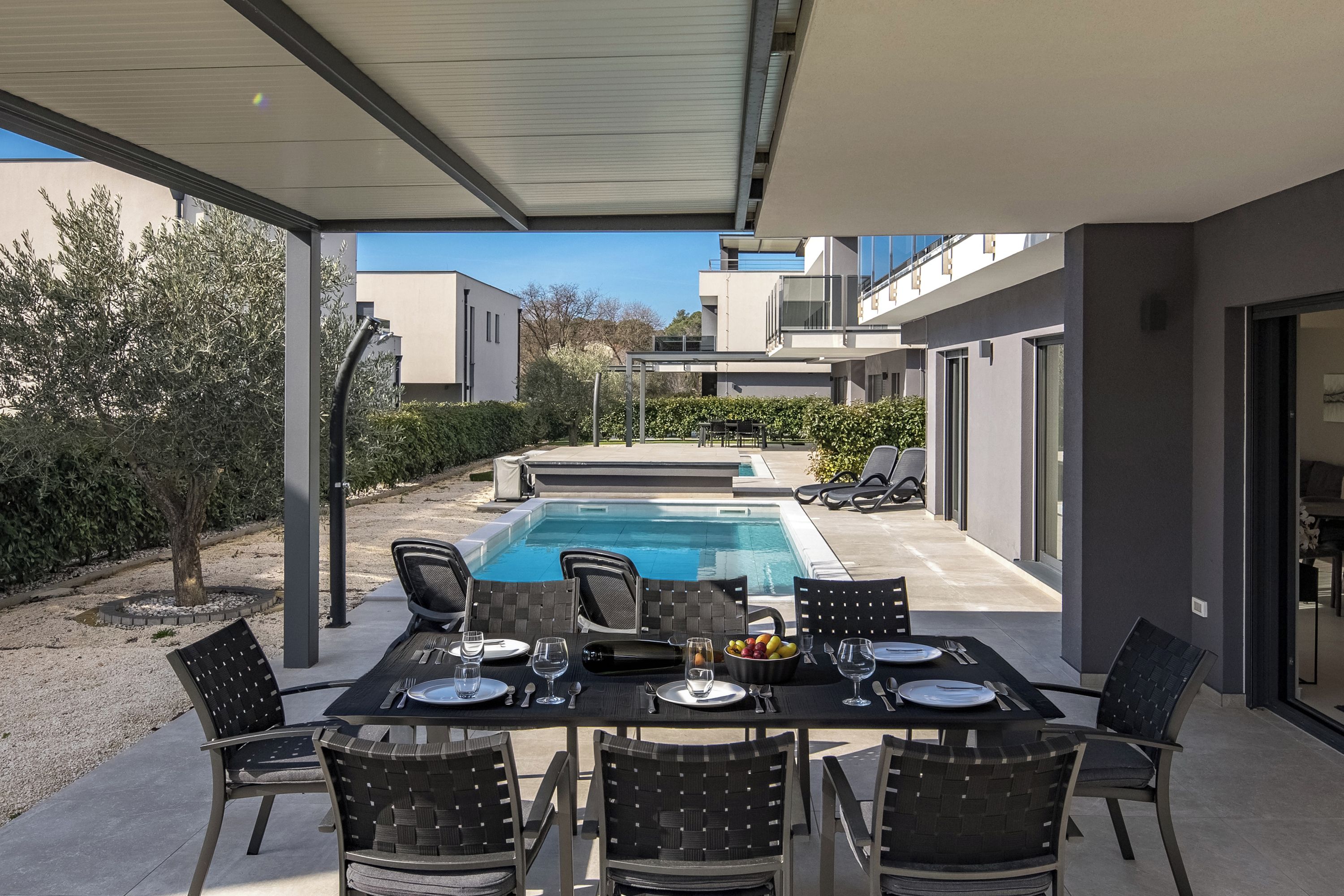 Un área de comedor al aire libre con piscina, arquitectura moderna y una vista despejada del paisaje circundante.