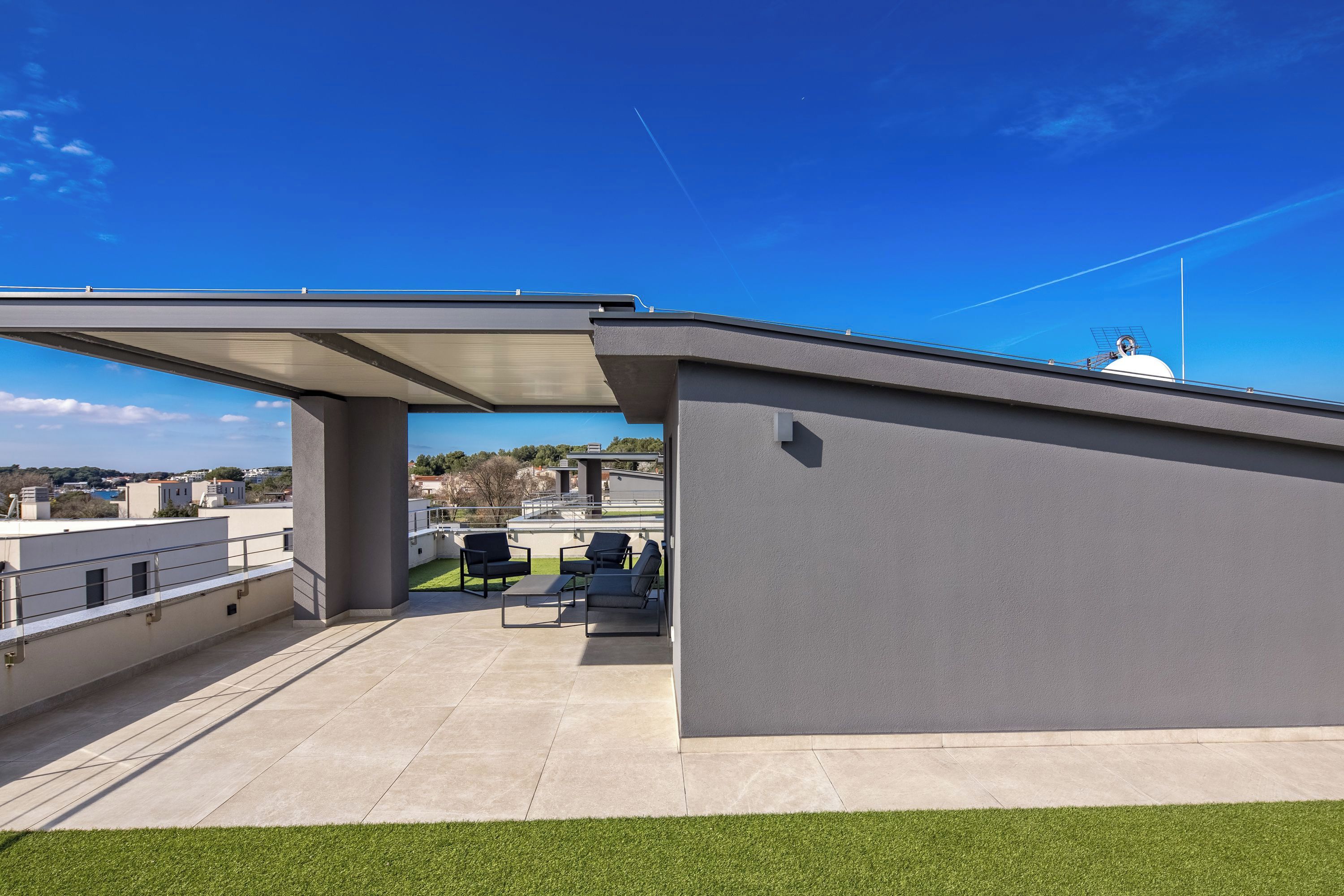A rooftop terrace with a covered seating area, a white dome structure, and a clear blue sky.