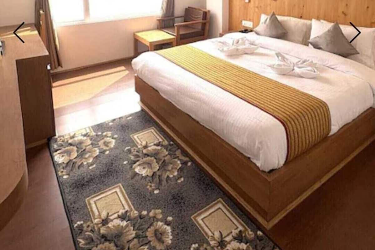 A hotel room with a bed, a desk, a chair, a ceiling fan, and a window with curtains.