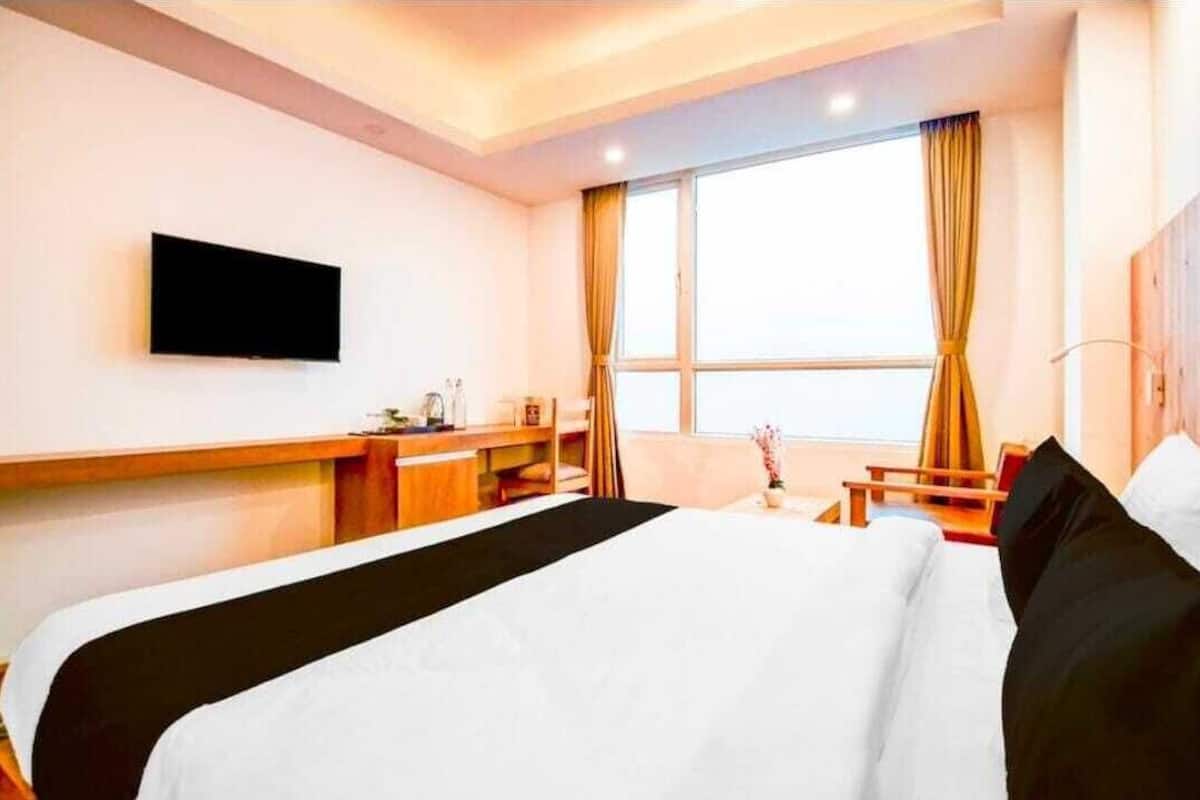 A hotel room with a bed, a desk, a chair, a TV, and a window with curtains.
